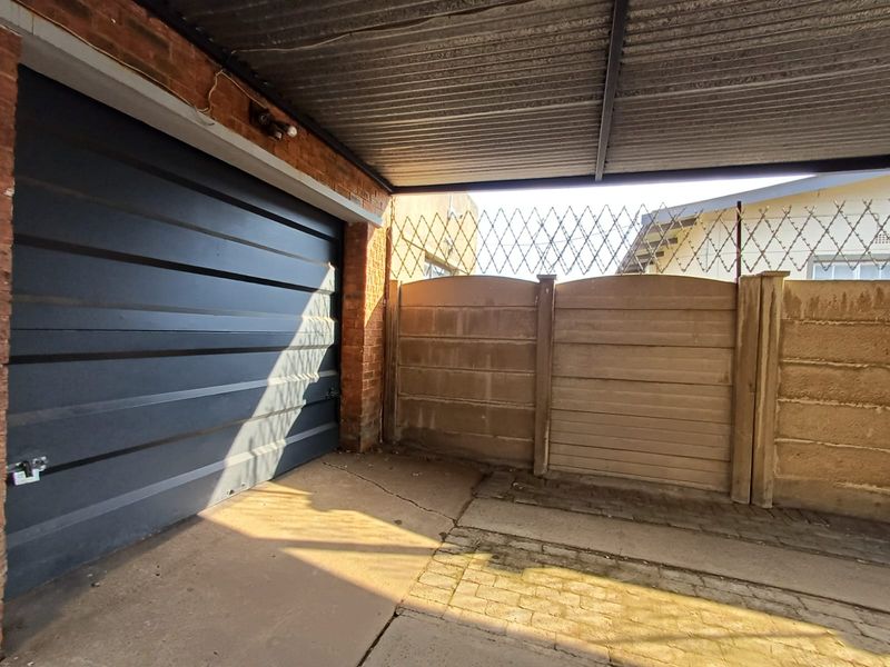 A covered garage area featuring a sectional door, corrugated metal roofing, and a concrete boundary wall topped with security razor wire.