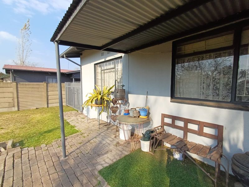 A covered outdoor patio area featuring paved flooring, a corrugated metal roof, and steel window frames, providing a functional space for outdoor relaxation.