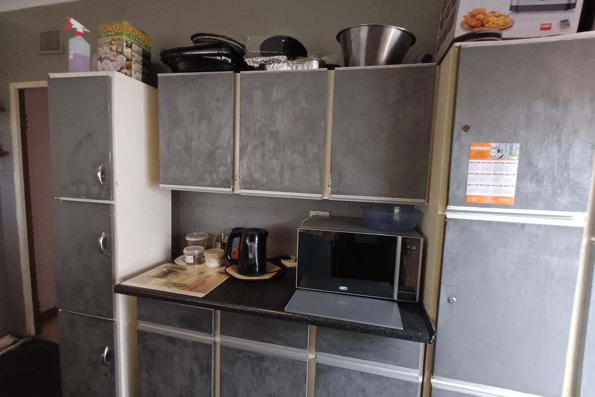 A functional kitchen area featuring built-in cabinetry, laminate countertops, and integrated storage space, currently showing signs of wear and dated finishes.