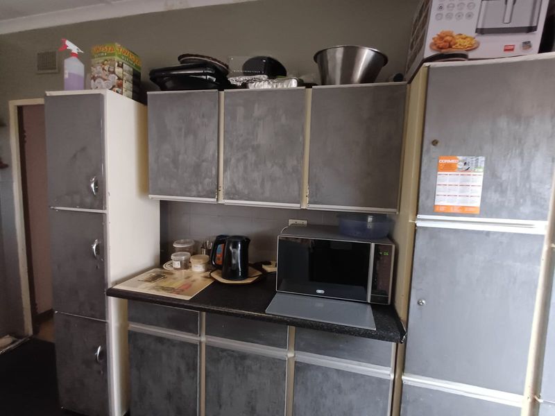 A functional kitchen area featuring built-in cabinetry, laminate countertops, and integrated storage space, currently showing signs of wear and dated finishes.