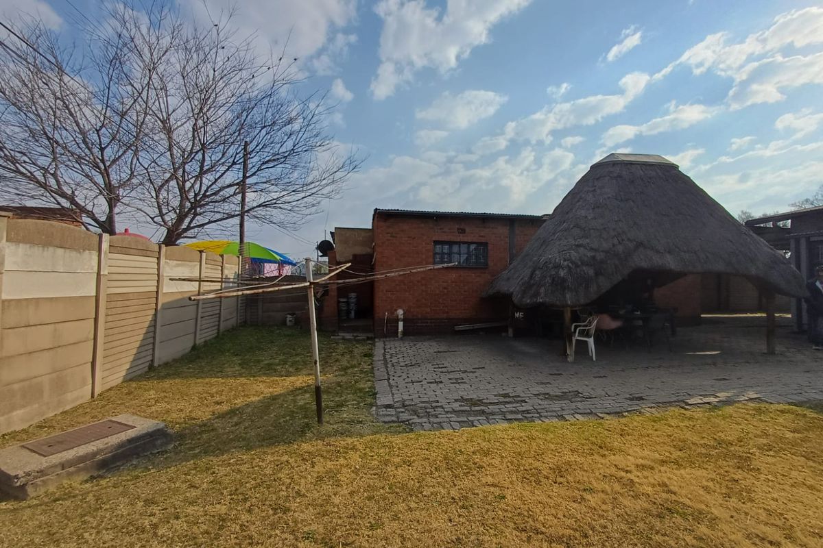 Rear garden area featuring a paved patio, a traditional thatched lapa, and a precast concrete boundary wall.