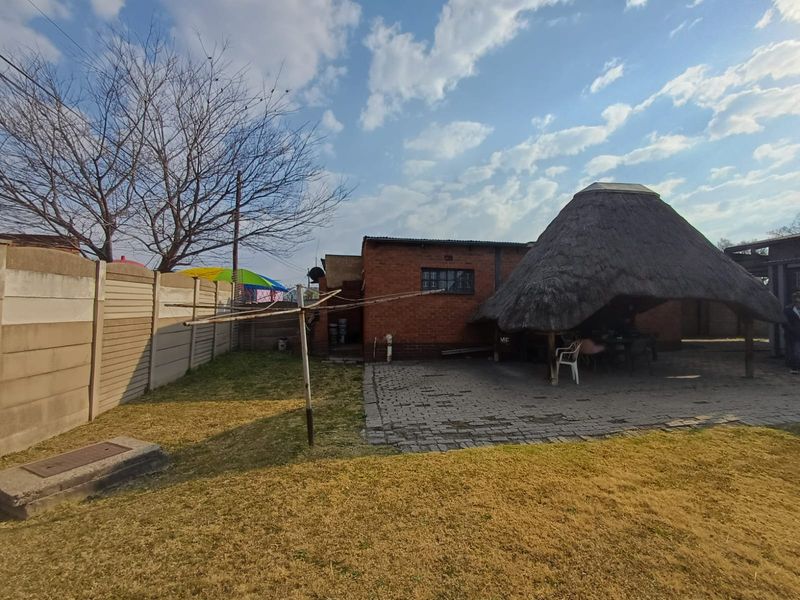 Rear garden area featuring a paved patio, a traditional thatched lapa, and a precast concrete boundary wall.