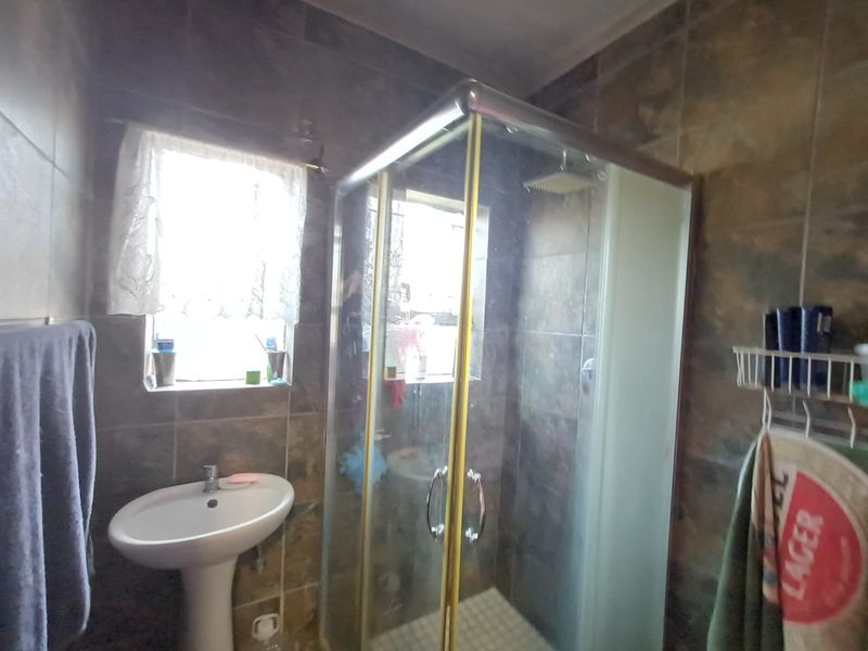 A functional bathroom featuring a pedestal basin and a corner shower enclosure with full-height wall tiling.
