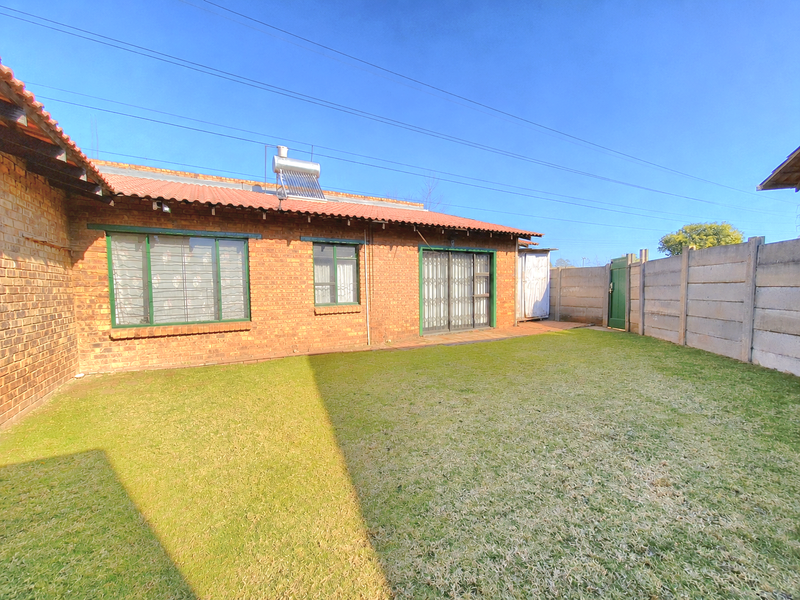 Rear view of a face brick house featuring a tiled roof, solar water heater, sliding door access, and a private garden with precast boundary walls.