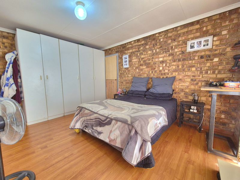 A bedroom featuring an exposed brick feature wall, laminate flooring, and a large built-in wardrobe providing ample storage space.