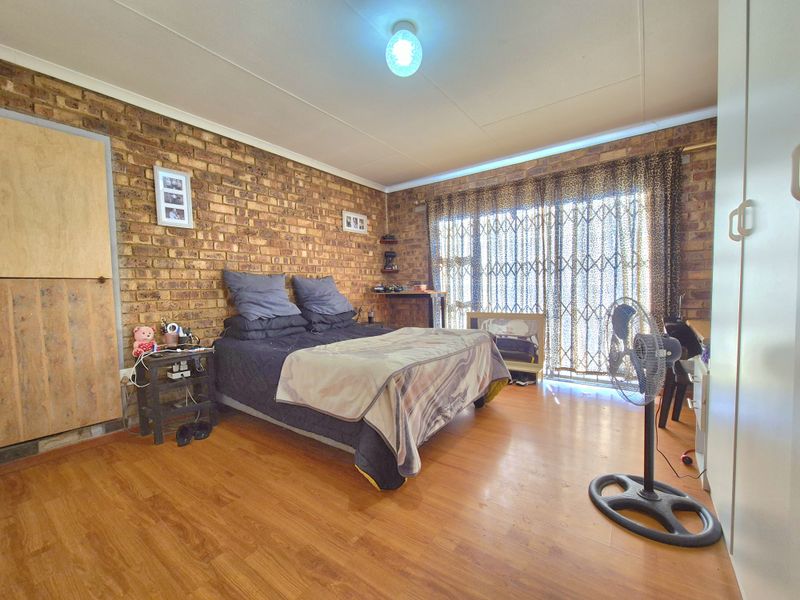A bedroom featuring an exposed brick feature wall, laminate flooring, and a sliding door with security gate leading to the exterior.