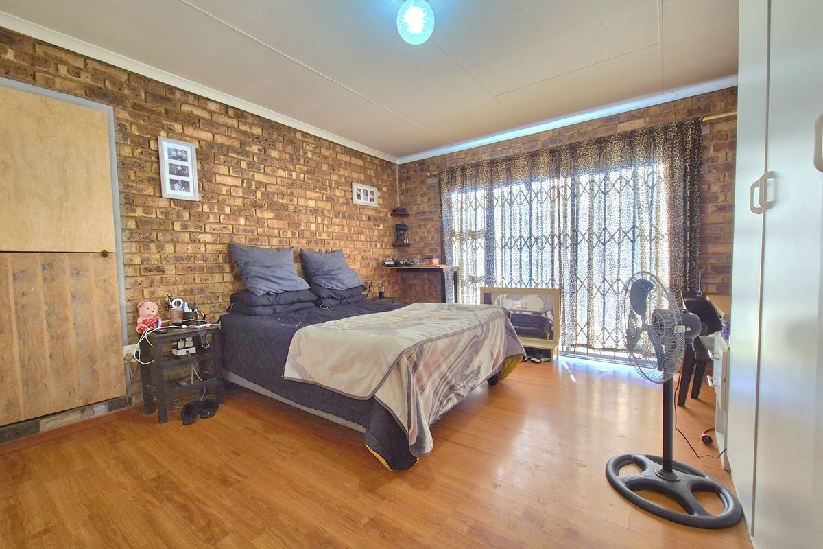 A bedroom featuring an exposed brick feature wall, laminate flooring, and a sliding door with security gate leading to the exterior.
