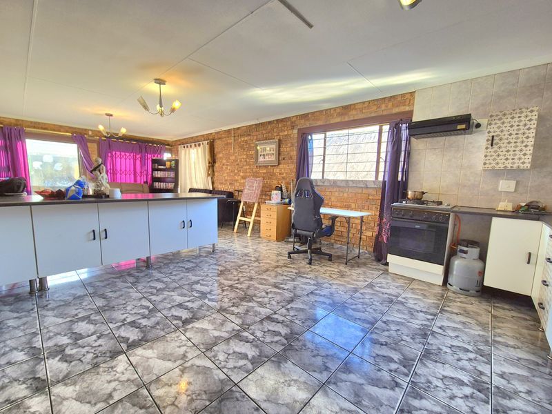 Spacious open-plan kitchen and living area featuring exposed brick walls, tiled flooring, a central kitchen island, and a freestanding oven with extractor fan.