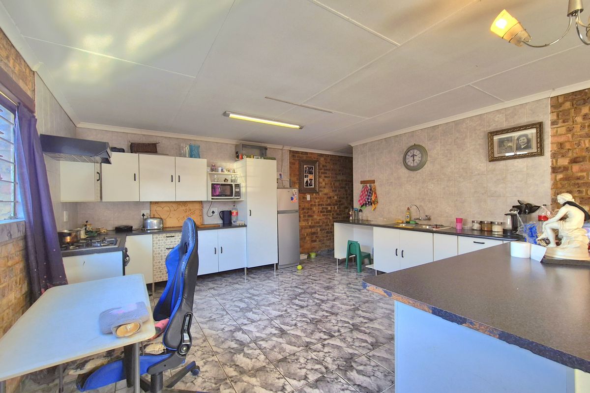 Spacious kitchen featuring exposed brick walls, tiled flooring, built-in cabinetry, and a gas hob, offering a functional layout with potential for modern updates.