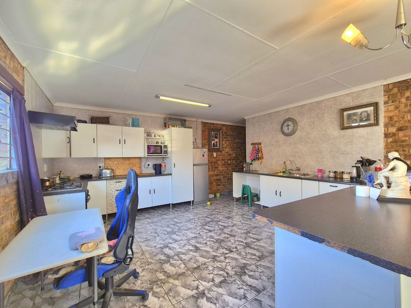 Spacious kitchen featuring exposed brick walls, tiled flooring, built-in cabinetry, and a gas hob, offering a functional layout with potential for modern updates.