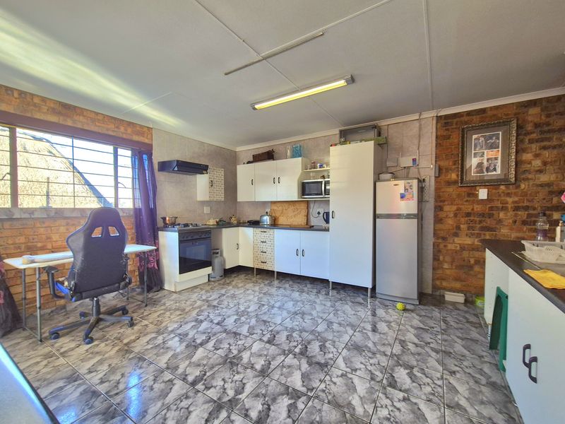 A functional kitchen featuring exposed brick walls, tiled flooring, and built-in cabinetry with a freestanding stove and extractor fan.