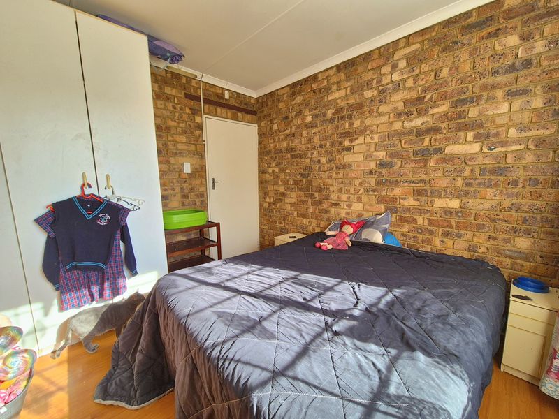 A bedroom featuring an exposed brick feature wall, laminate flooring, and a built-in wardrobe.