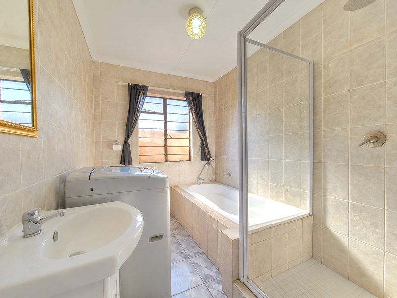 A functional bathroom featuring a pedestal basin, a built-in bathtub, and a separate glass-enclosed shower with neutral wall and floor tiling.