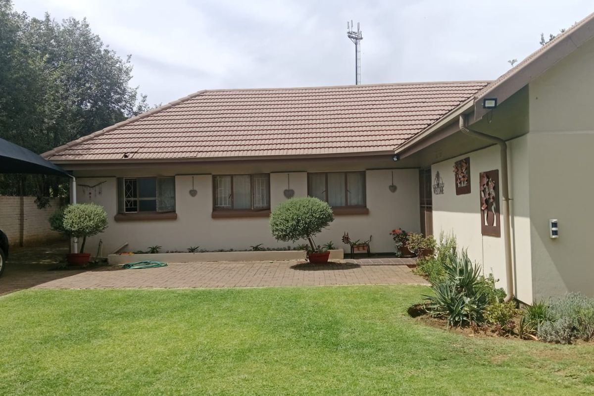 A rear view of the house featuring a tiled roof, paved patio area, and a well-maintained lawn.