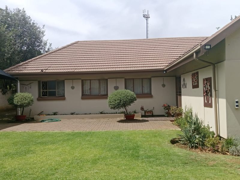 A rear view of the house featuring a tiled roof, paved patio area, and a well-maintained lawn.
