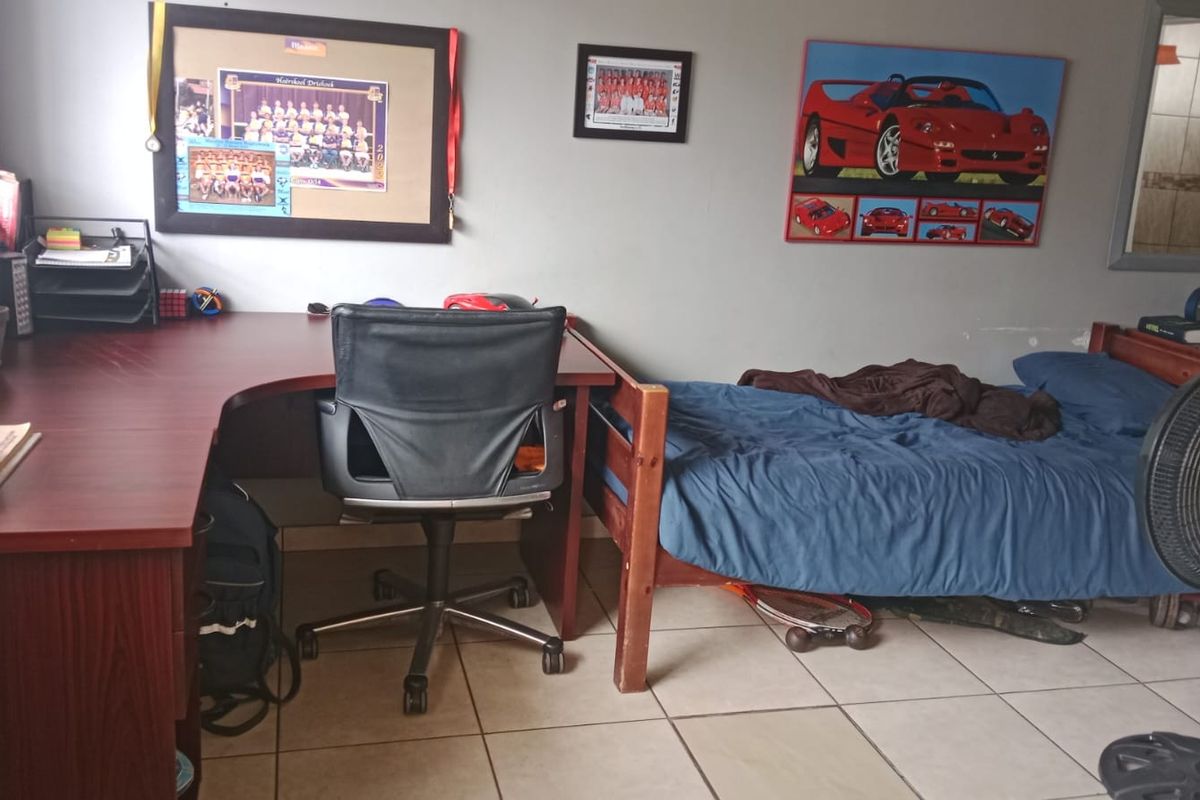 A functional bedroom featuring tiled flooring and window blinds, currently utilized as a combined sleeping and study space.