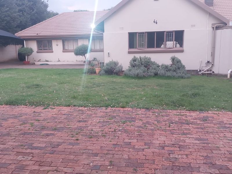 Front view of a single-story house featuring a brick driveway, lawn, and carport, with security bars on the windows.