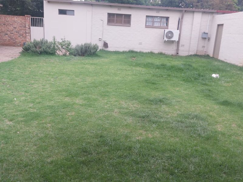 A rear garden area featuring a lawn, paved walkway, and brick boundary walls, with an exterior air conditioning unit mounted on the building wall.