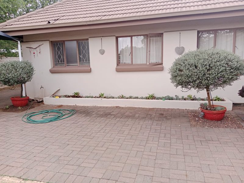 Rear exterior view of the property featuring a paved patio area, raised garden bed, and tiled roof structure with security-fitted windows.