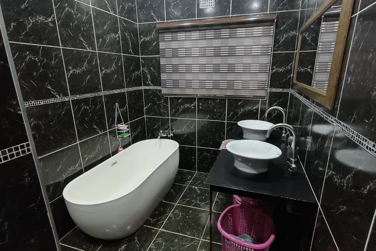 Modern bathroom featuring a freestanding bathtub, dual vessel sinks with chrome fixtures, and striking black marble-effect wall and floor tiling.