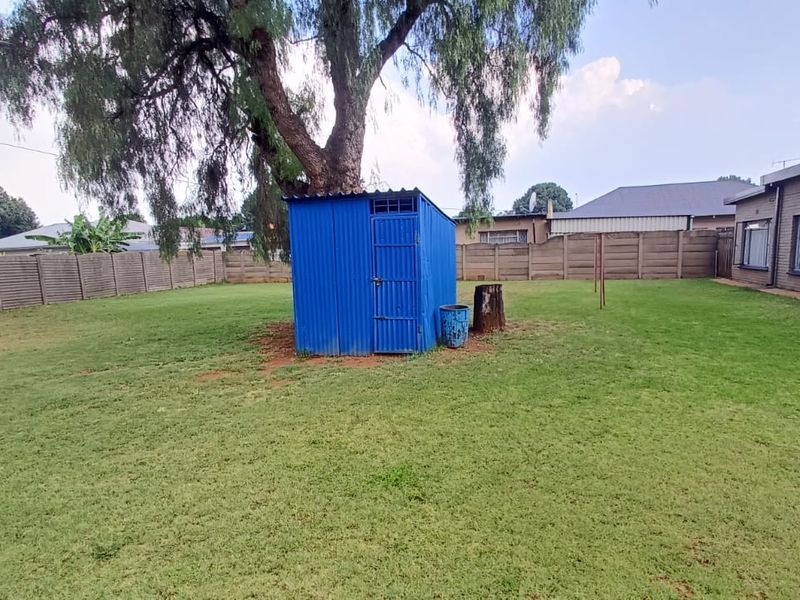 Spacious backyard featuring a large mature tree, a corrugated metal storage shed, and perimeter precast concrete walling.