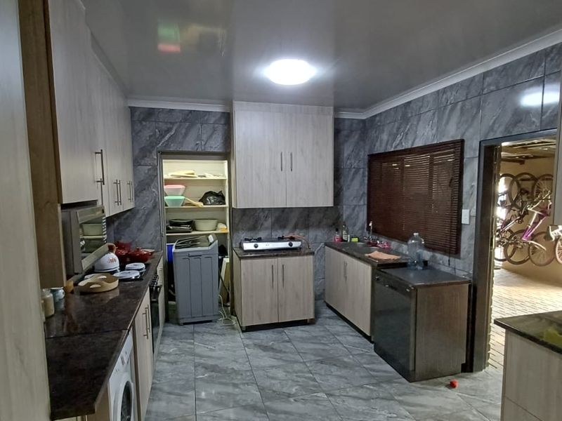 A functional kitchen featuring light wood-finish cabinetry, granite countertops, tiled wall finishes, and a dedicated pantry area with integrated appliances.
