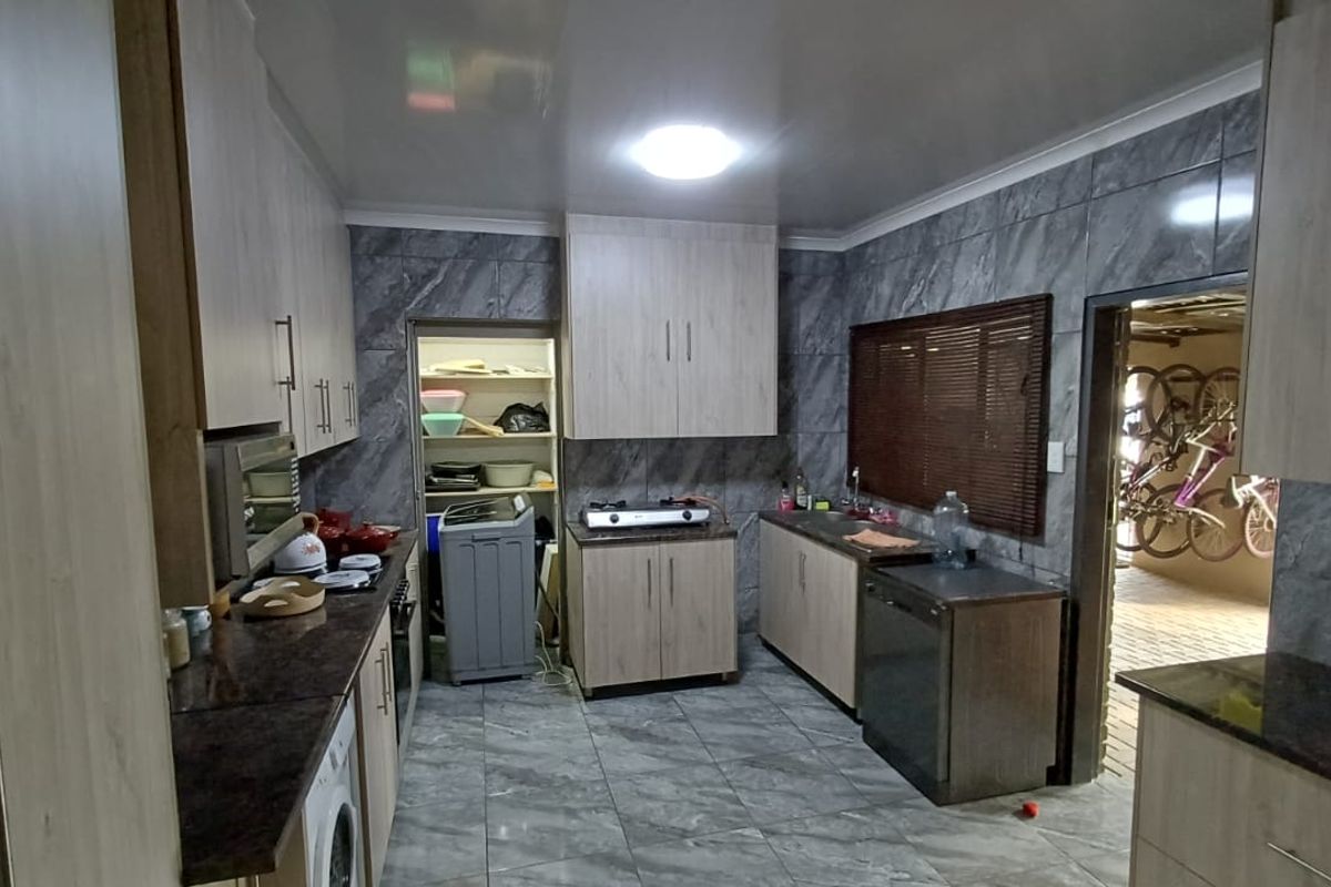 A functional kitchen featuring light wood-finish cabinetry, granite countertops, tiled wall finishes, and a dedicated pantry area with integrated appliances.