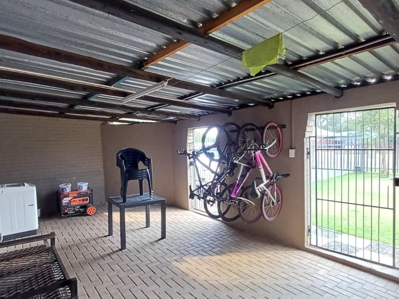 A covered outdoor patio area featuring brick paving, exposed timber rafters, and secure metal gates, suitable for use as a utility or entertainment space.