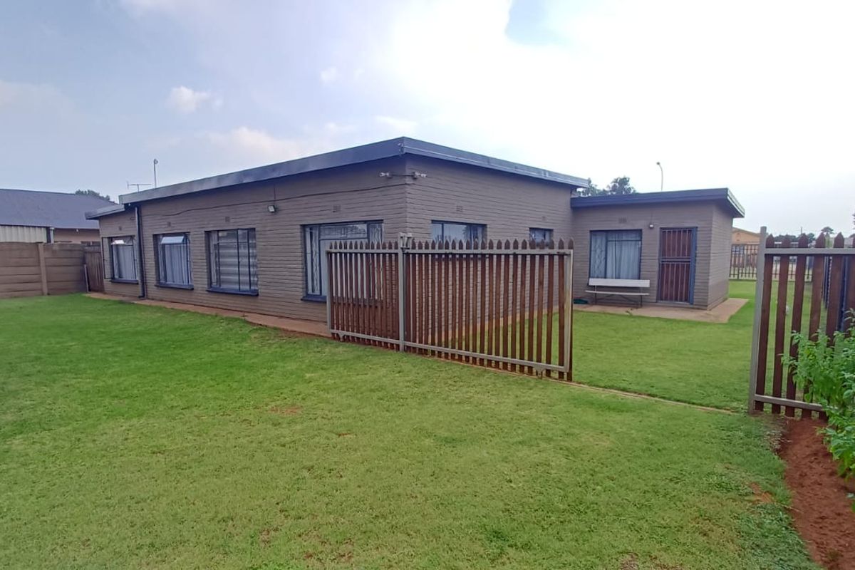 Rear view of the property featuring a brick facade, secure perimeter fencing, and a well-maintained lawn area.