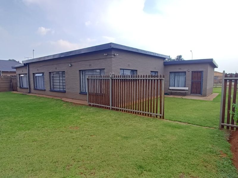 Rear view of the property featuring a brick facade, secure perimeter fencing, and a well-maintained lawn area.