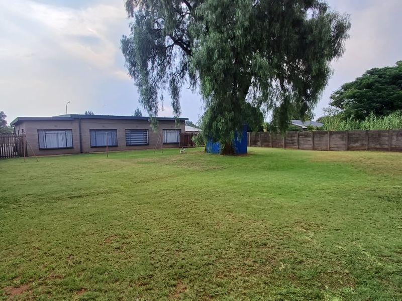 Spacious rear garden featuring a large established tree, expansive lawn area, and secure precast concrete boundary walling.