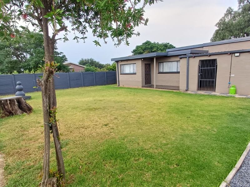 A view of the rear exterior of the house featuring a lawn, perimeter fencing, and secure gated access points.