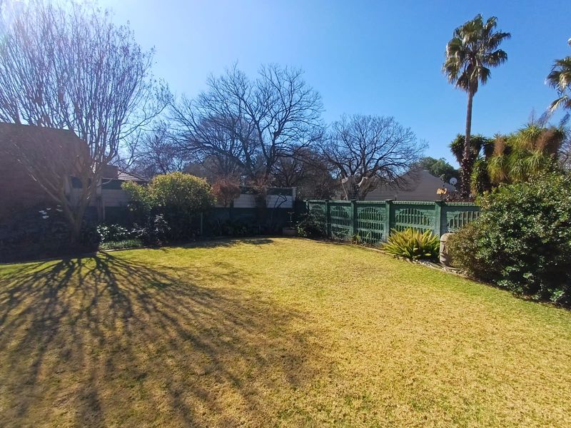 A spacious, well-maintained private garden featuring a manicured lawn, mature trees, and established perimeter fencing.
