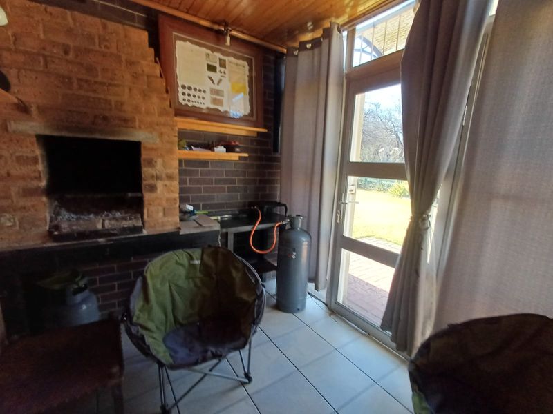 Covered patio area featuring a built-in brick fireplace, tiled flooring, and a timber ceiling with direct access to the garden.