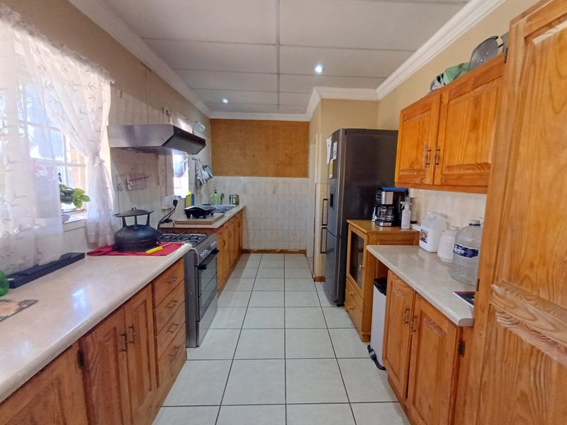 A functional kitchen featuring wooden cabinetry, laminate countertops, a freestanding stove with extractor fan, and tiled flooring, requiring some cosmetic updates.