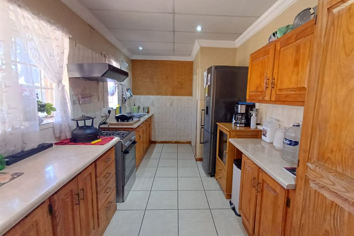 A functional kitchen featuring wooden cabinetry, laminate countertops, a freestanding stove with extractor fan, and tiled flooring, requiring some cosmetic updates.