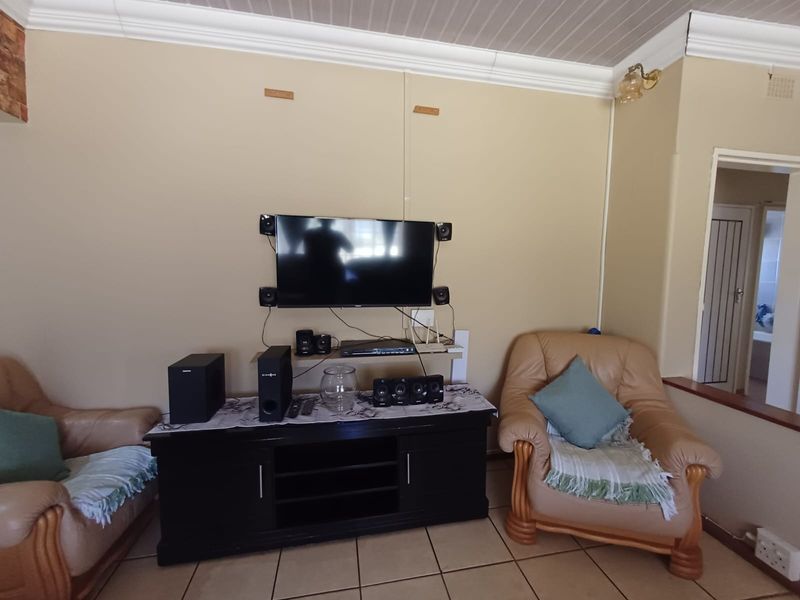 A living room featuring tiled flooring and coved ceiling details, currently set up as a media area with wall-mounted television infrastructure.