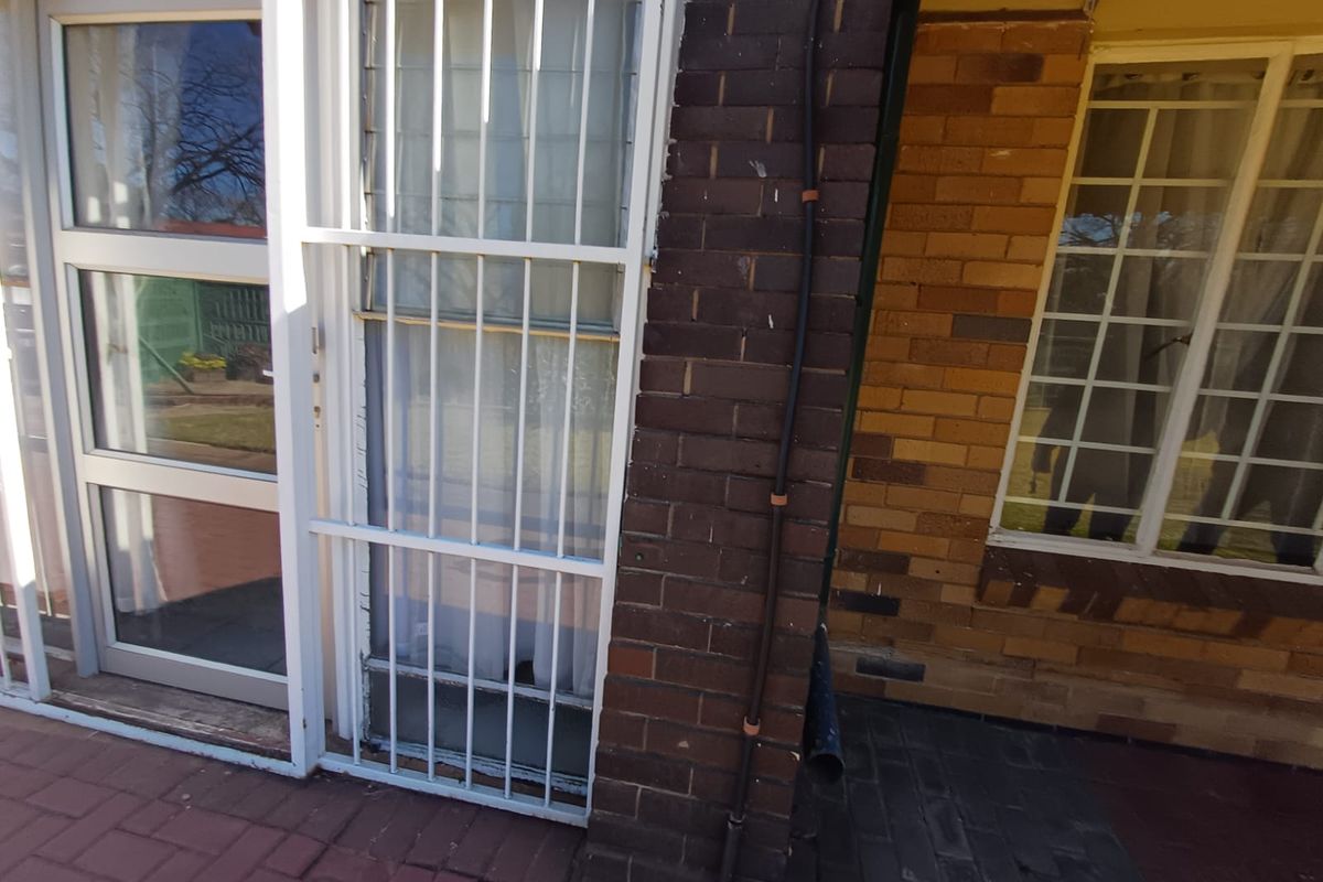 A view of the rear exterior featuring brick wall construction, paved patio area, and security bars on the windows.