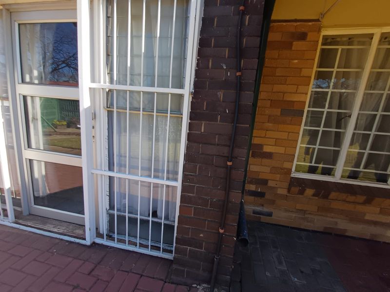 A view of the rear exterior featuring brick wall construction, paved patio area, and security bars on the windows.