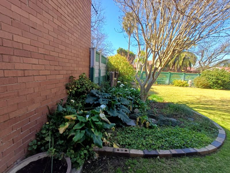 A well-established rear garden featuring mature trees, landscaped garden beds with brick edging, and a combination of brick and precast concrete boundary fencing.