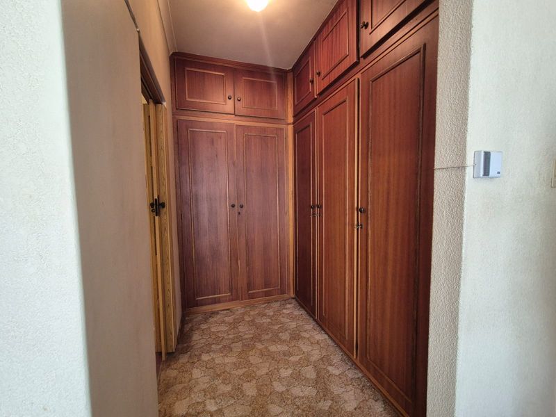 A hallway featuring extensive built-in wooden cabinetry with overhead storage and patterned carpet flooring.
