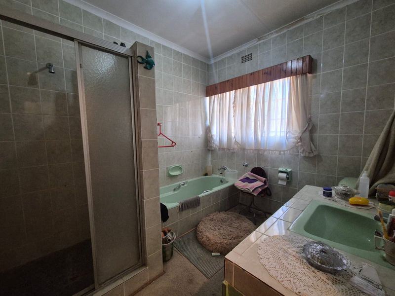 A dated bathroom featuring a built-in bathtub, separate shower enclosure, and tiled vanity area, offering potential for a modern renovation.