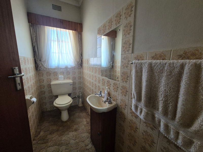 A compact bathroom featuring dated floral wall tiles, a wall-mounted basin with vanity cabinet, and a standard toilet.