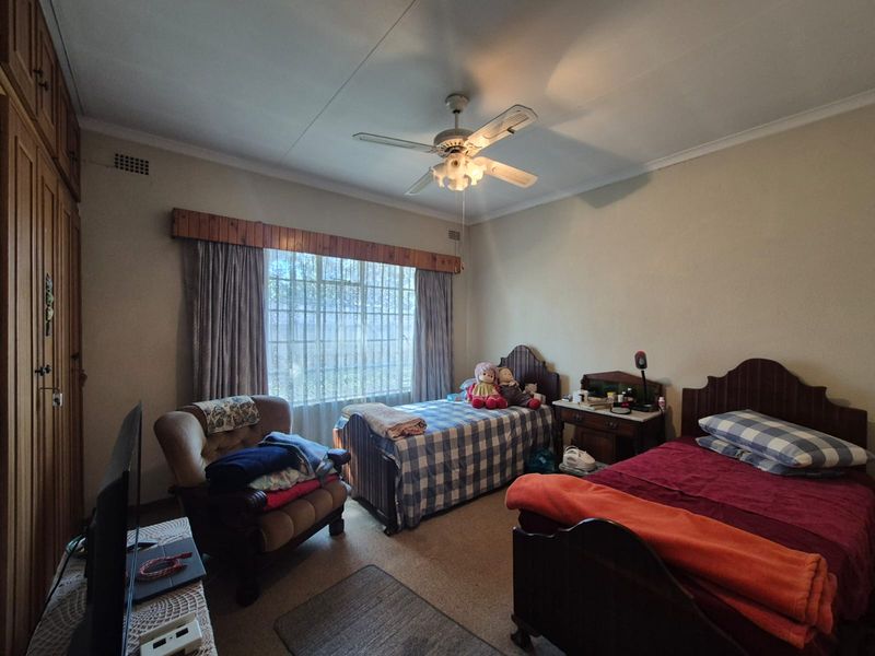 A spacious bedroom featuring built-in wooden cupboards, a ceiling fan, and large windows, offering a functional layout with potential for modern updates.