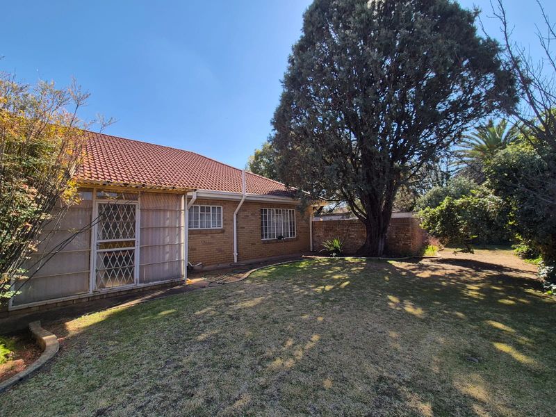 Rear view of the house featuring a brick facade, tiled roof, security gates, and a spacious garden area with mature trees.