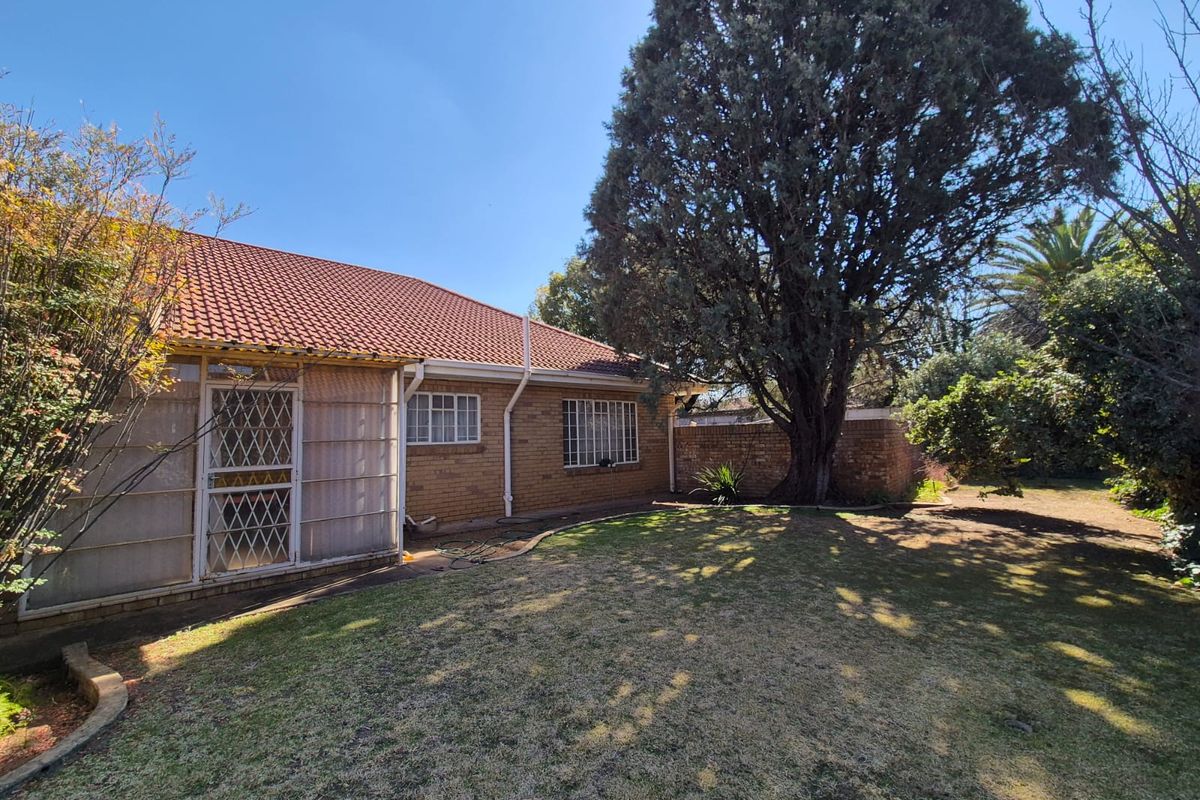 Rear view of the house featuring a brick facade, tiled roof, security gates, and a spacious garden area with mature trees.