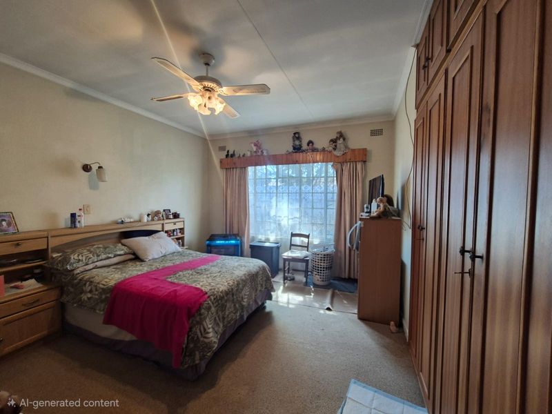 A bedroom featuring built-in wooden cupboards, a ceiling fan, and a large window, offering a functional space with traditional finishes.
