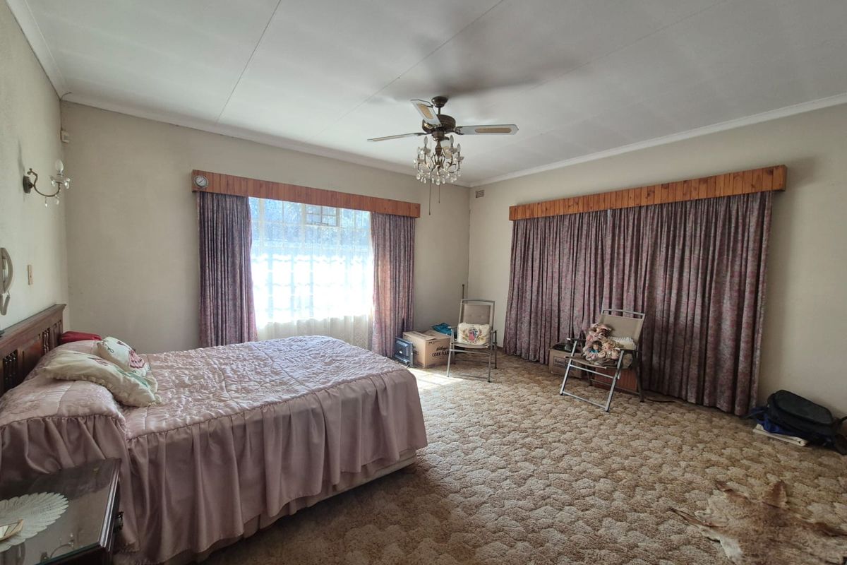 Spacious bedroom featuring a ceiling fan, crystal chandelier, and timber curtain pelmets, offering a dated interior ready for modernization.