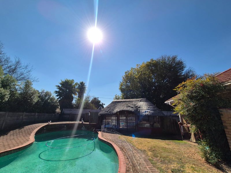 Outdoor pool area featuring a swimming pool, brick paved surround, and a traditional thatched lapa structure in the rear garden.