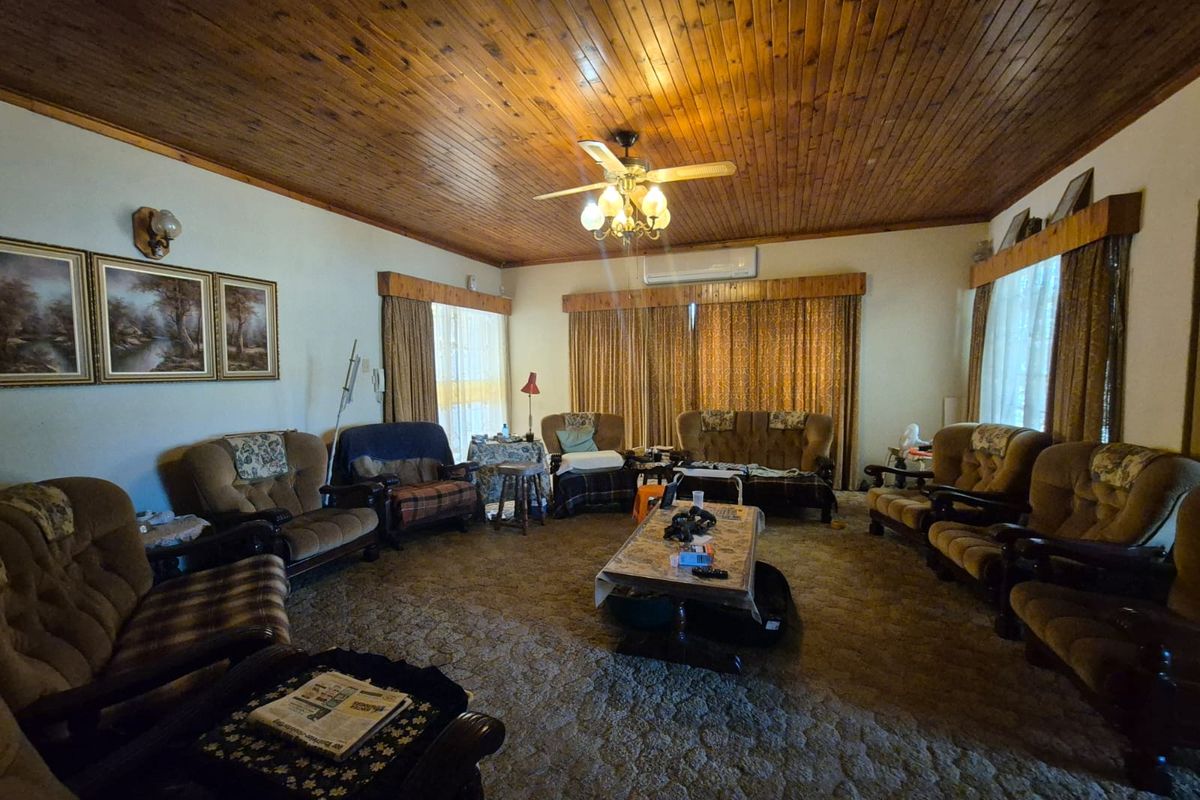 Spacious living room featuring a timber-clad ceiling, ceiling fan, and wall-mounted air conditioning unit, offering a dated aesthetic ready for modernization.